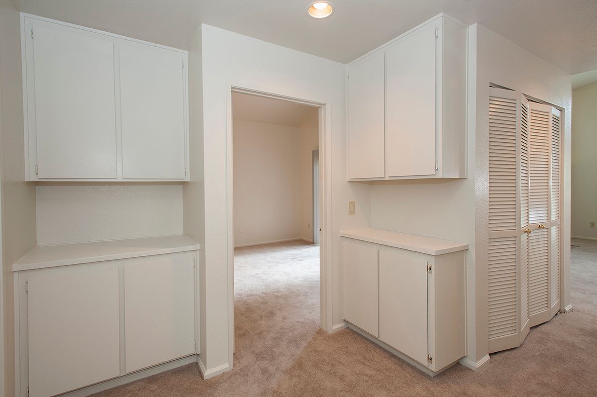 White built-in cabinets and closets in a carpeted apartment hallway.