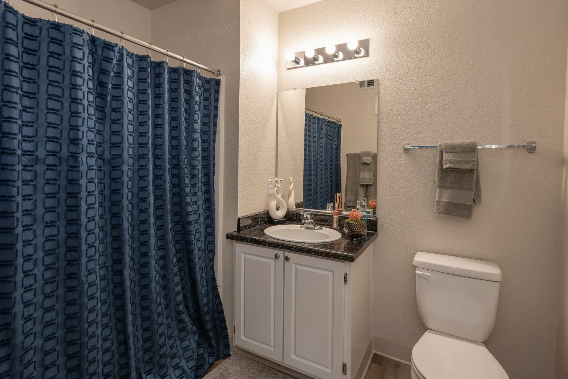Bathroom with vanity, sink, mirror, toilet, and blue shower curtain.