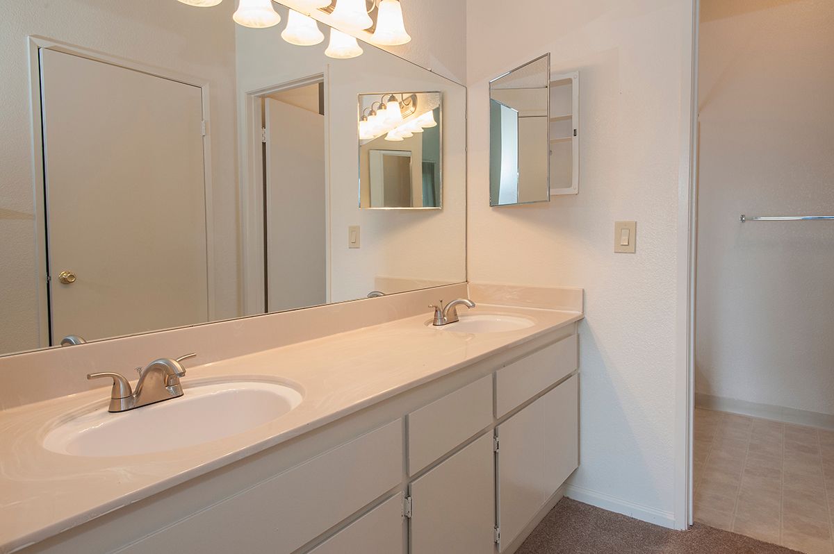 Bathroom with double-sink vanity, large mirror, and bright overhead lights.