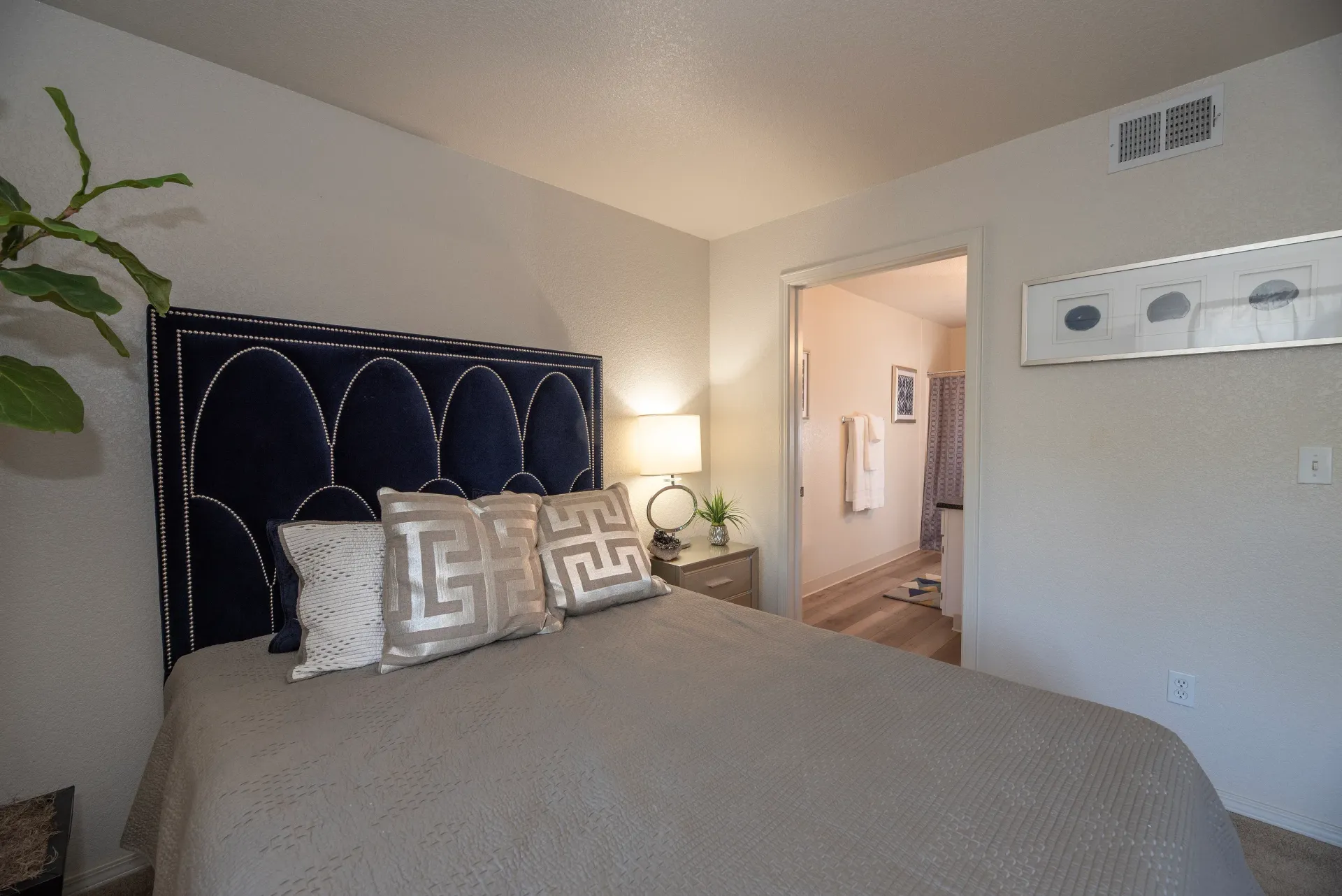 Bedroom with navy upholstered headboard, gray bedding, a nightstand with a lamp, and doorway to an en-suite bathroom.