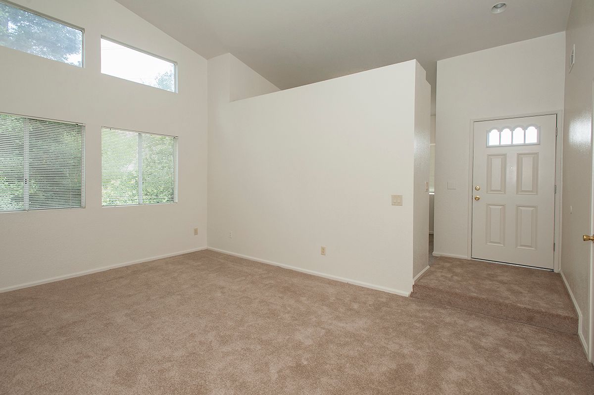 Empty apartment living room with beige carpet, white walls, and large windows by the entry door.