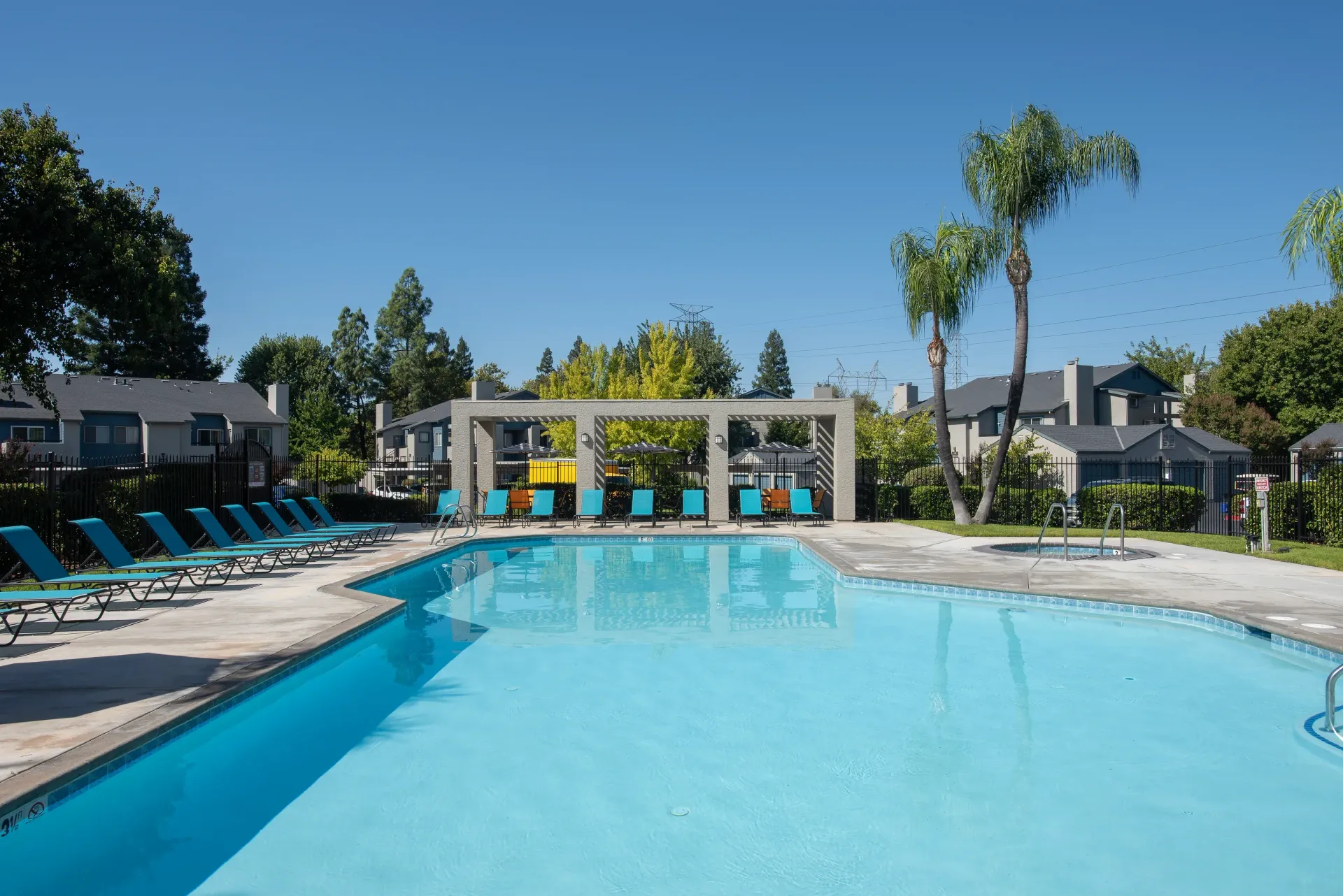 Outdoor apartment community pool with blue lounge chairs along the deck and a shaded seating area.