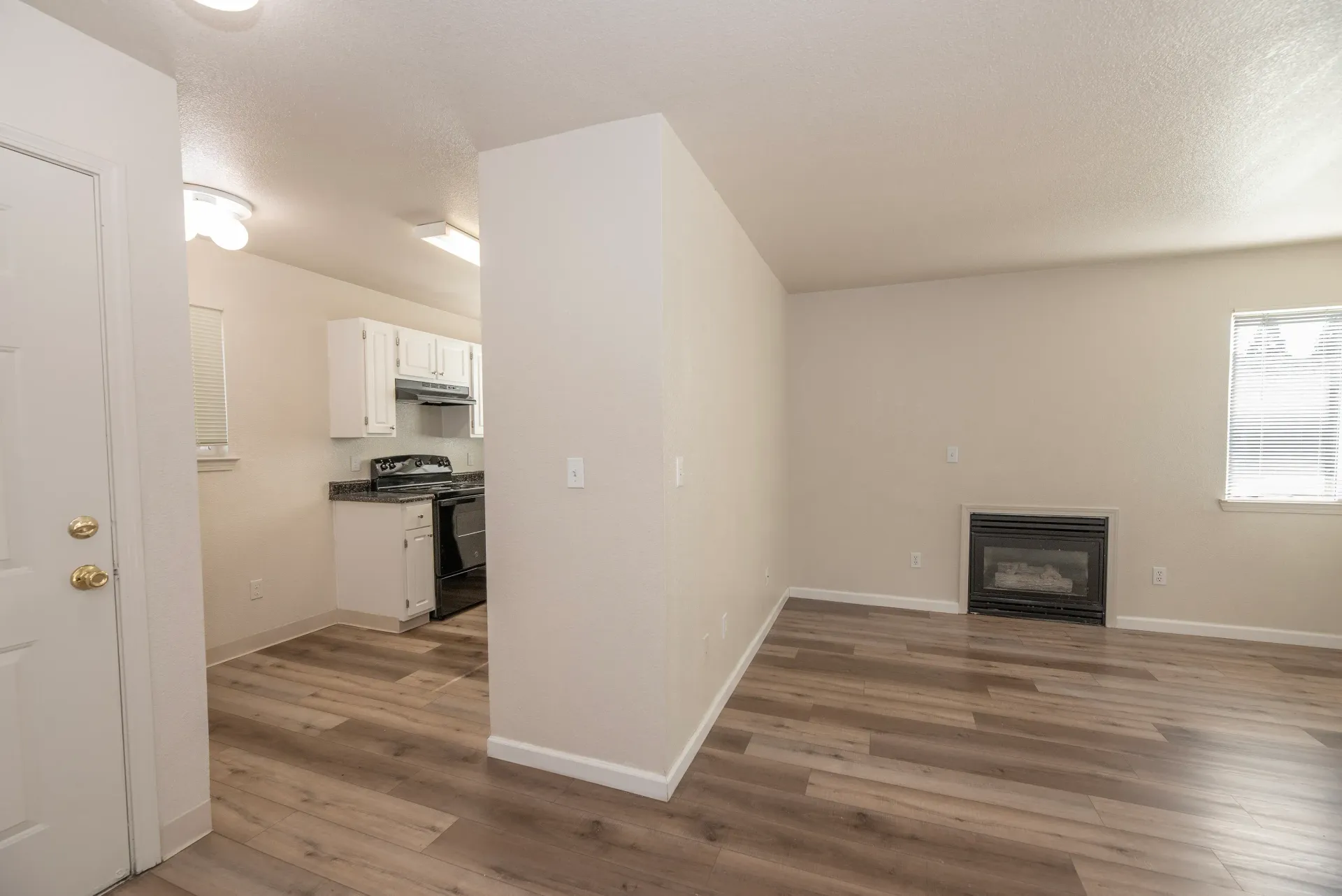 Open-concept living area with a kitchen to the left, a fireplace on the far wall, and wood-like flooring.