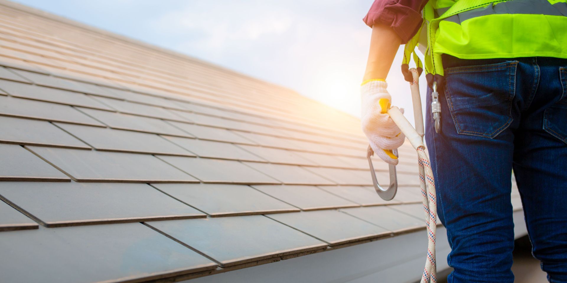 Person on a rooftop wearing safety gear, holding a carabiner.