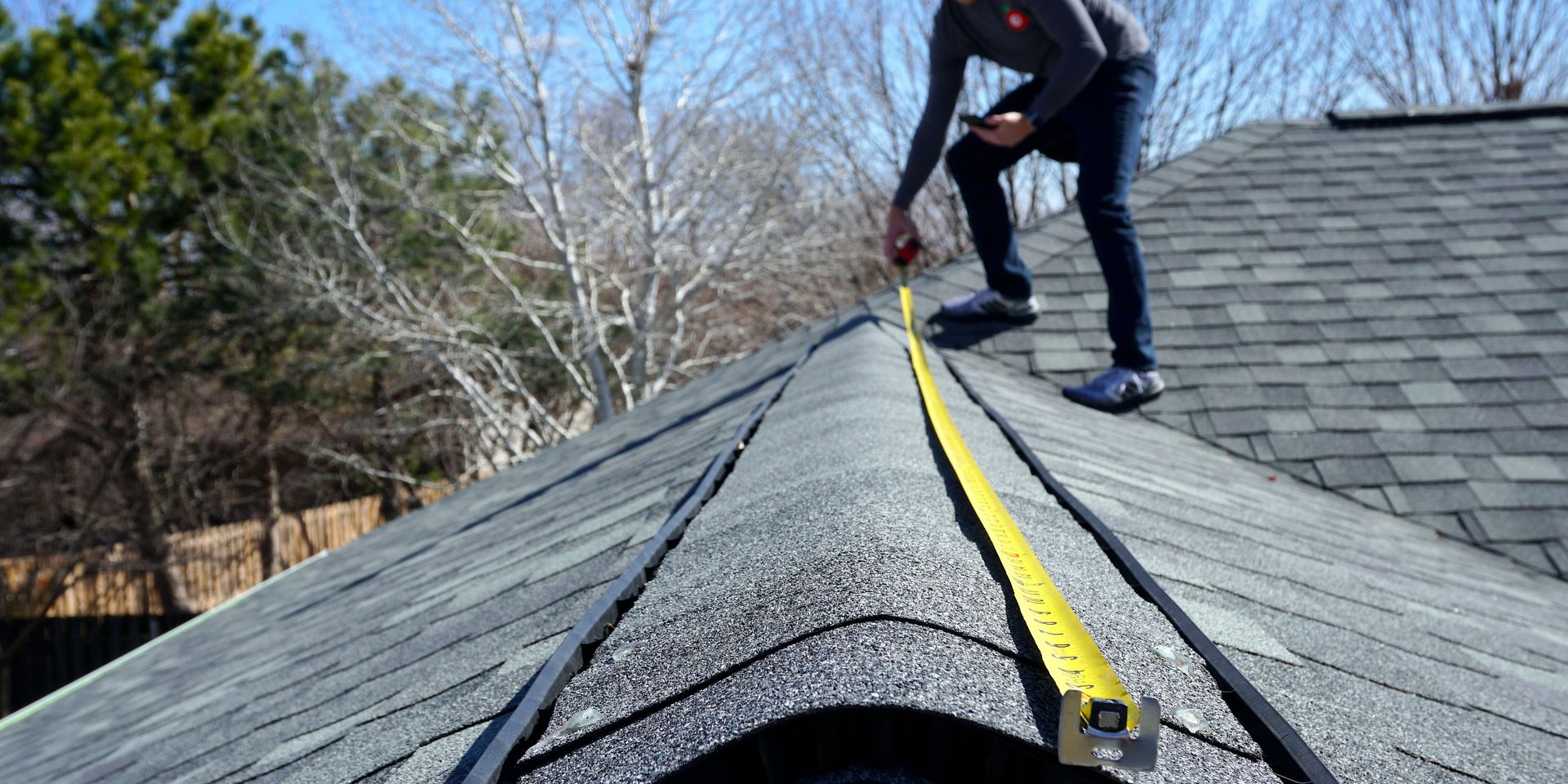A man is measuring the roof of a house with a tape measure.
