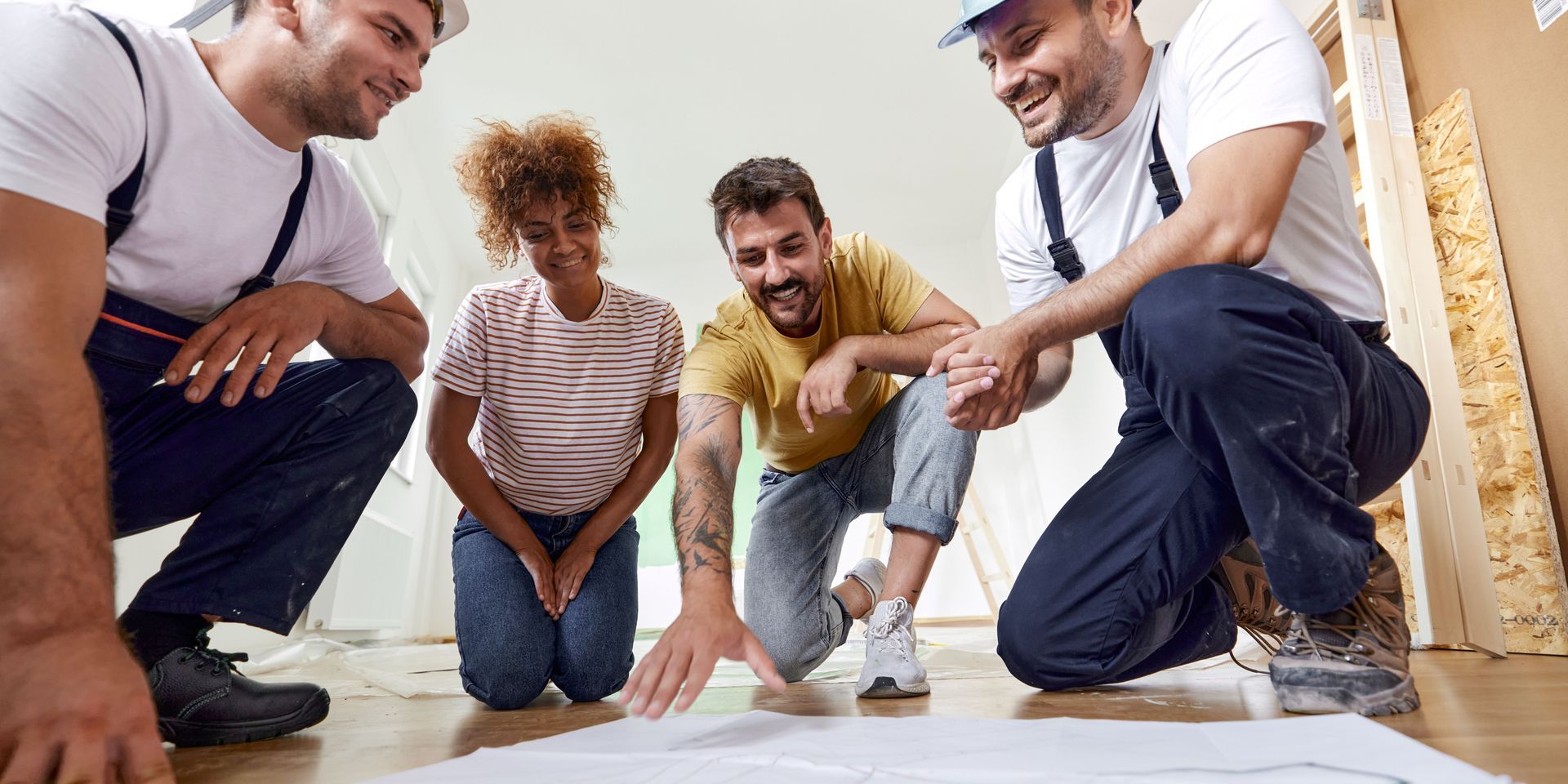 A group of construction workers are looking at a blueprint on the floor.