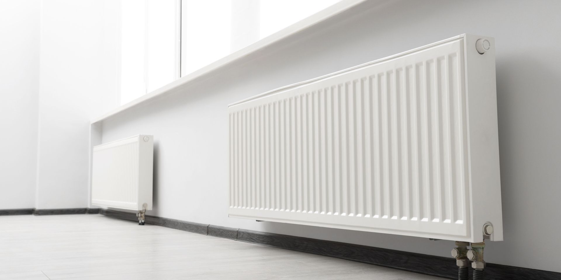 White radiators on a white wall near a window.