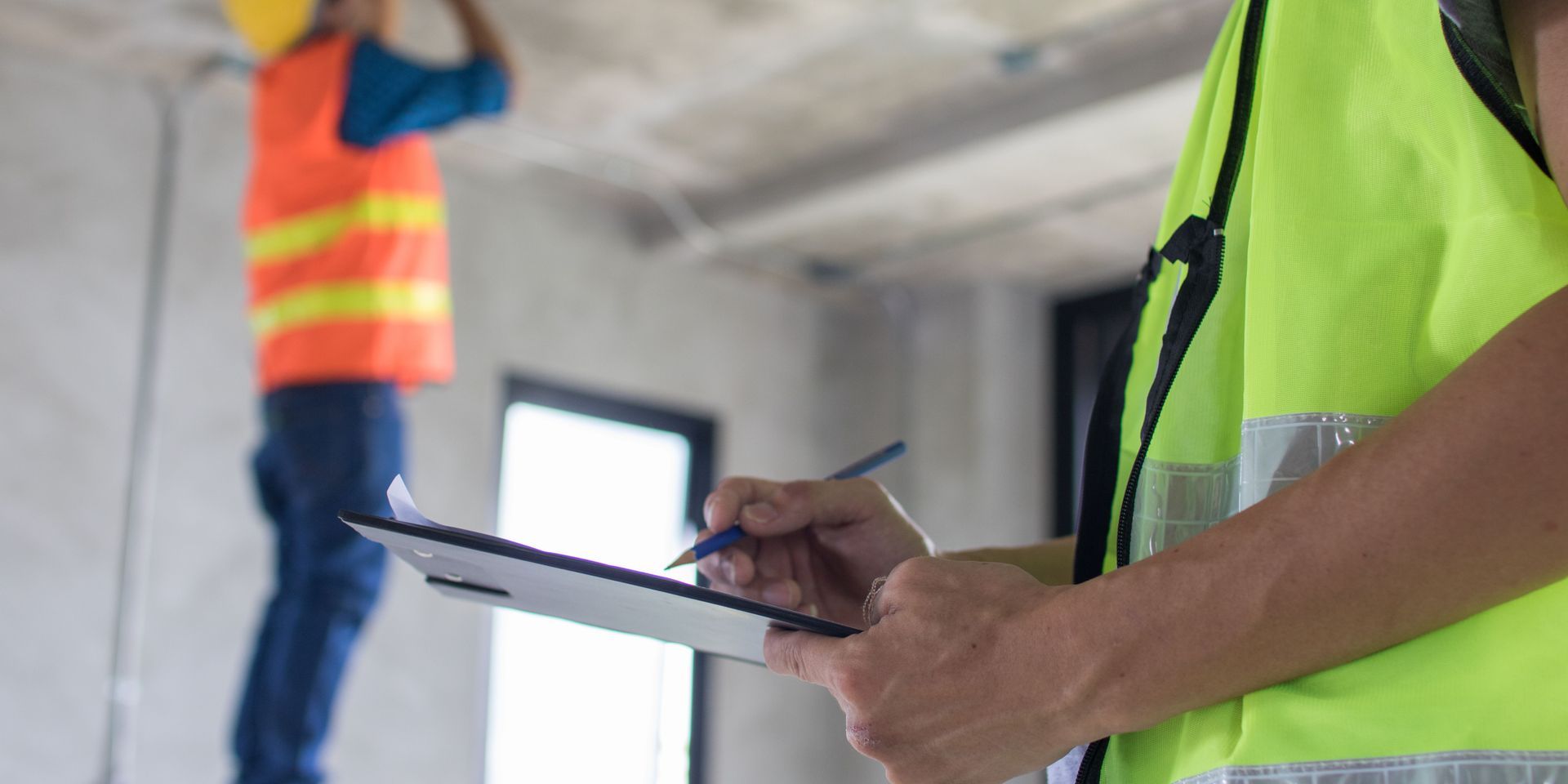 A construction worker is holding a clipboard and writing on it.