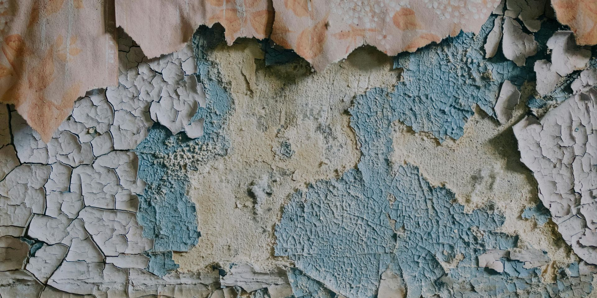 Cracked and peeling blue, beige, and white paint on a wall.
