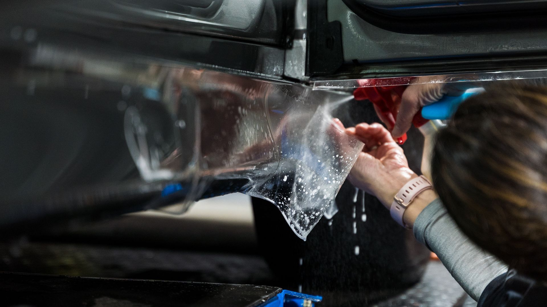 A woman is applying a protective film to the side of a car.
