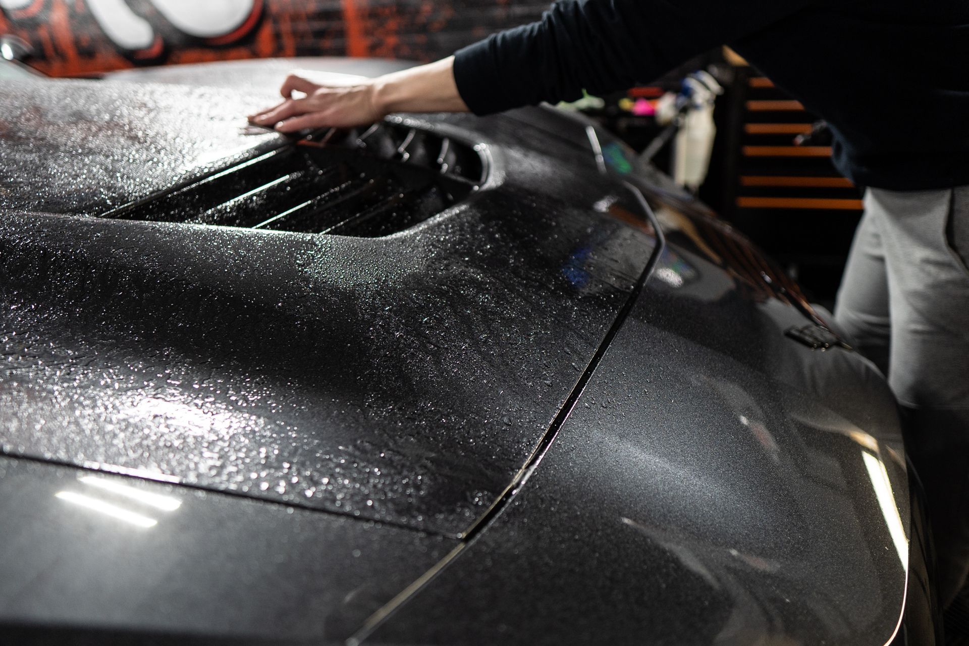 A person is cleaning the hood of a car in a garage.