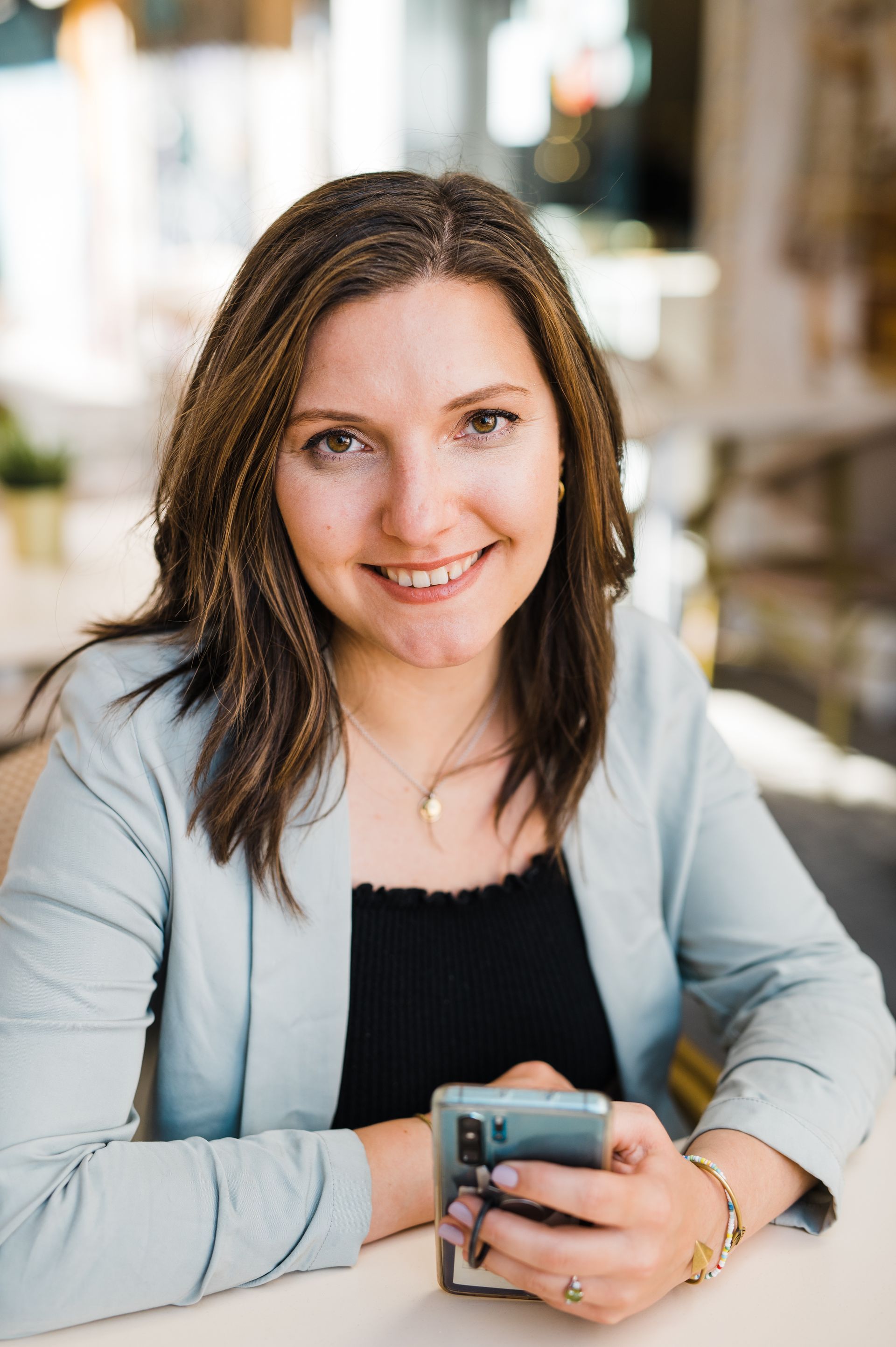 Smiling brown haired white women wearing a pale green blazer and black top