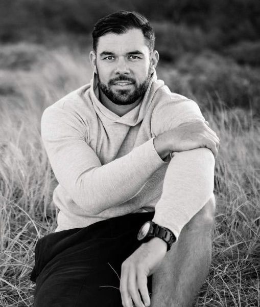 A man with a beard is sitting in the grass in a black and white photo.