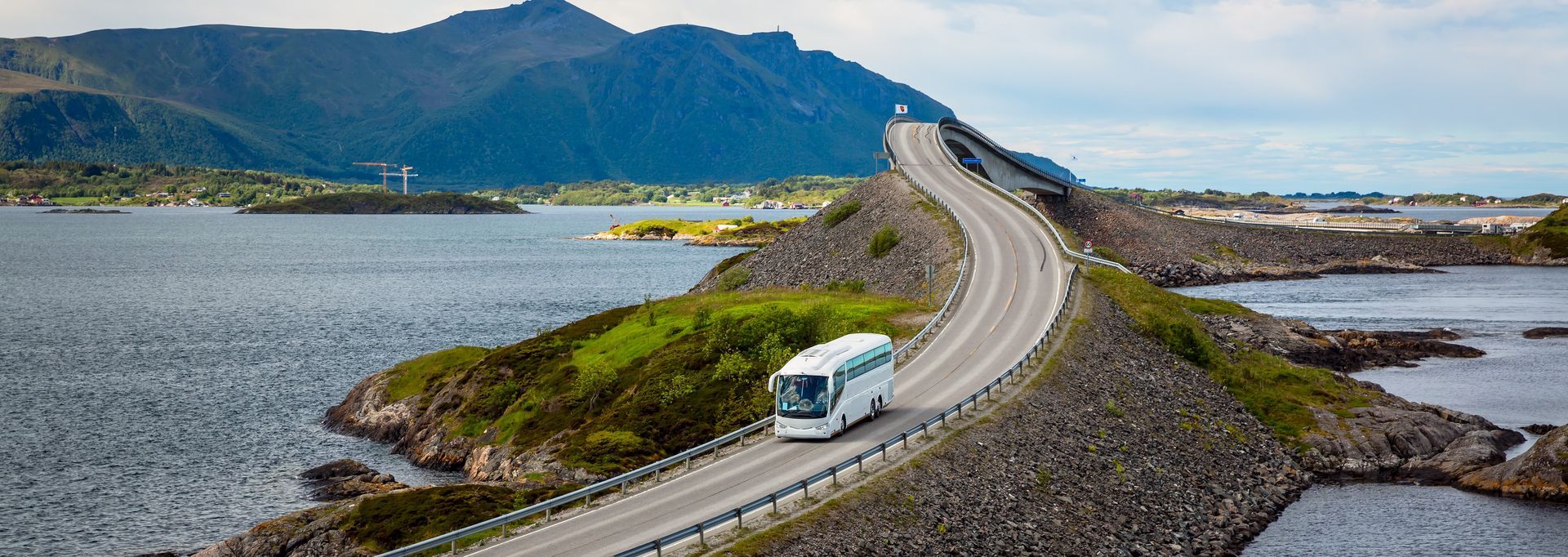 Een bus rijdt over een bergweg langs een meer.