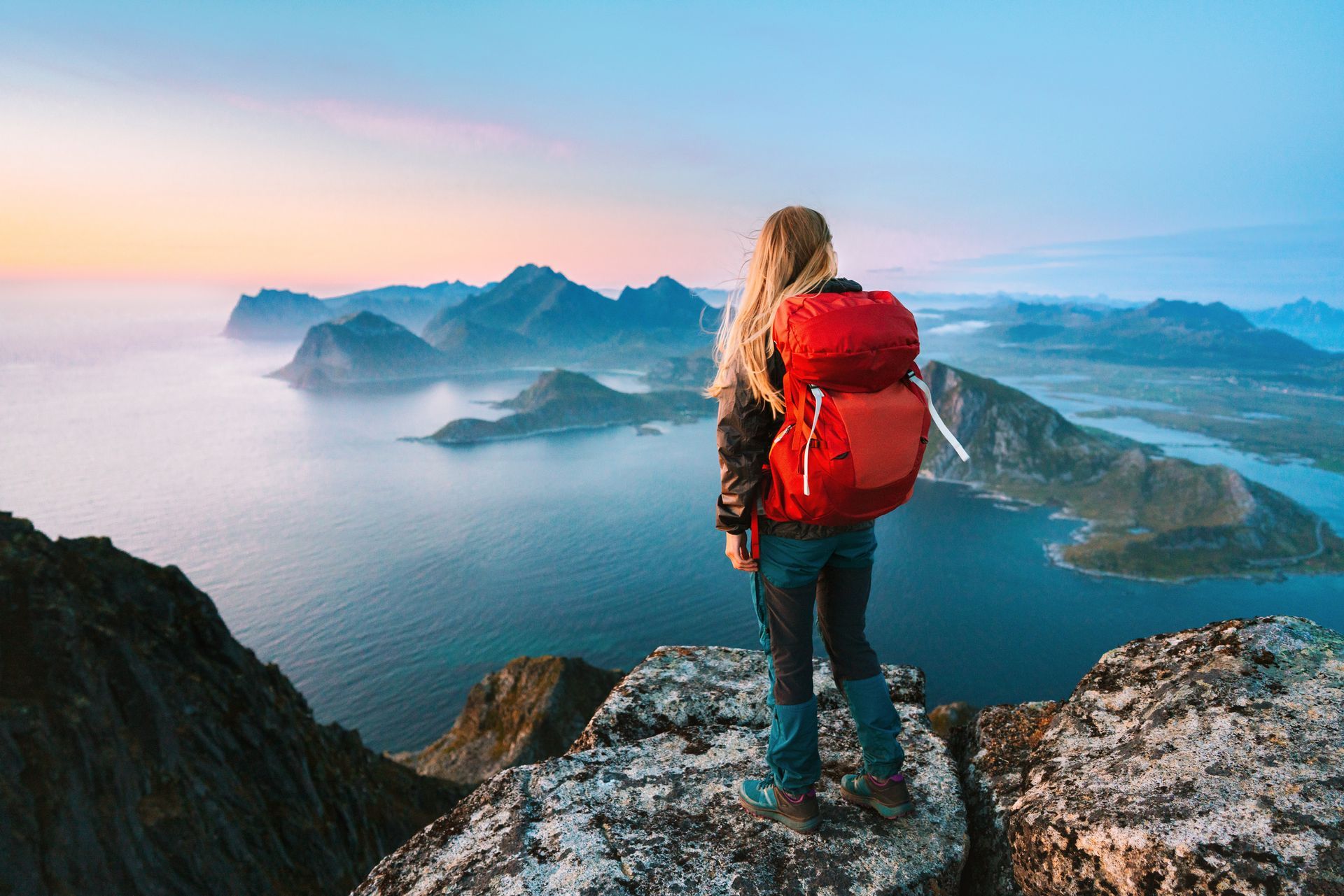 Een vrouw met een rugzak staat op de top van een berg met uitzicht op de oceaan.