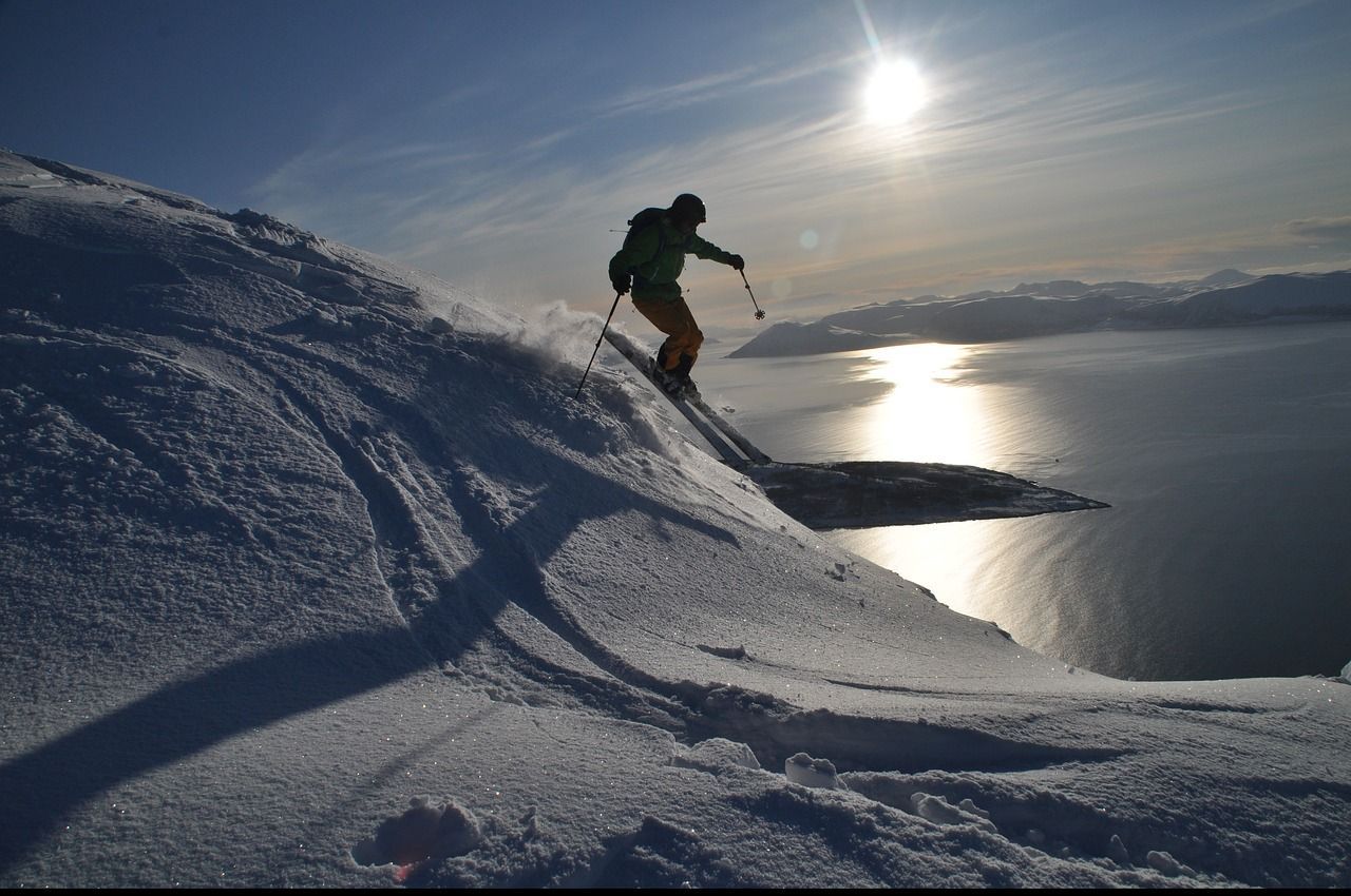 Een persoon skiet een met sneeuw bedekte helling af met uitzicht op een fjord.