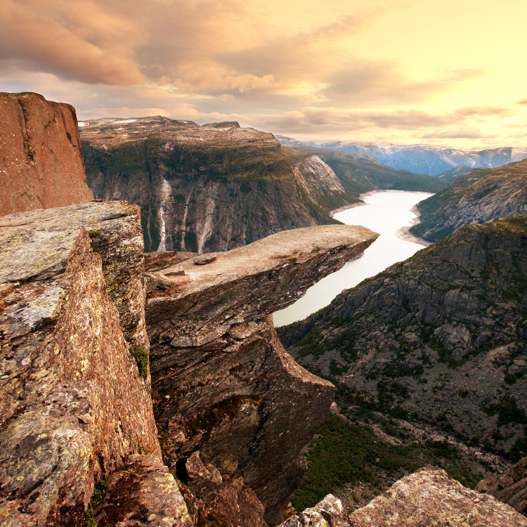 A person is standing on a rock overlooking a lake surrounded by mountains.