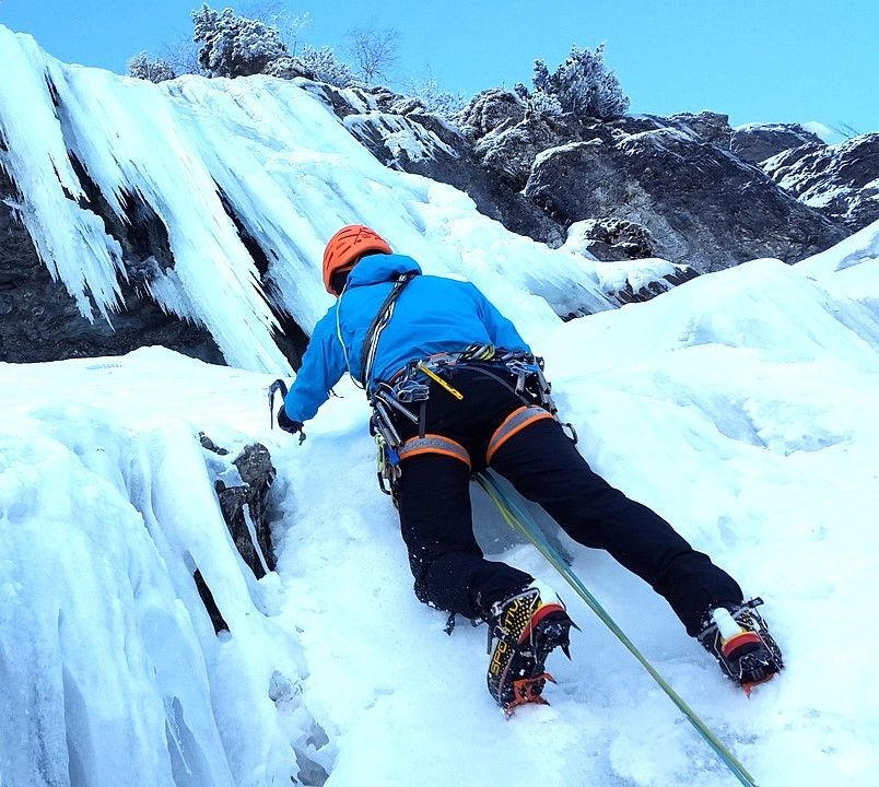 Een persoon in een blauw jasje beklimt een bevroren waterval