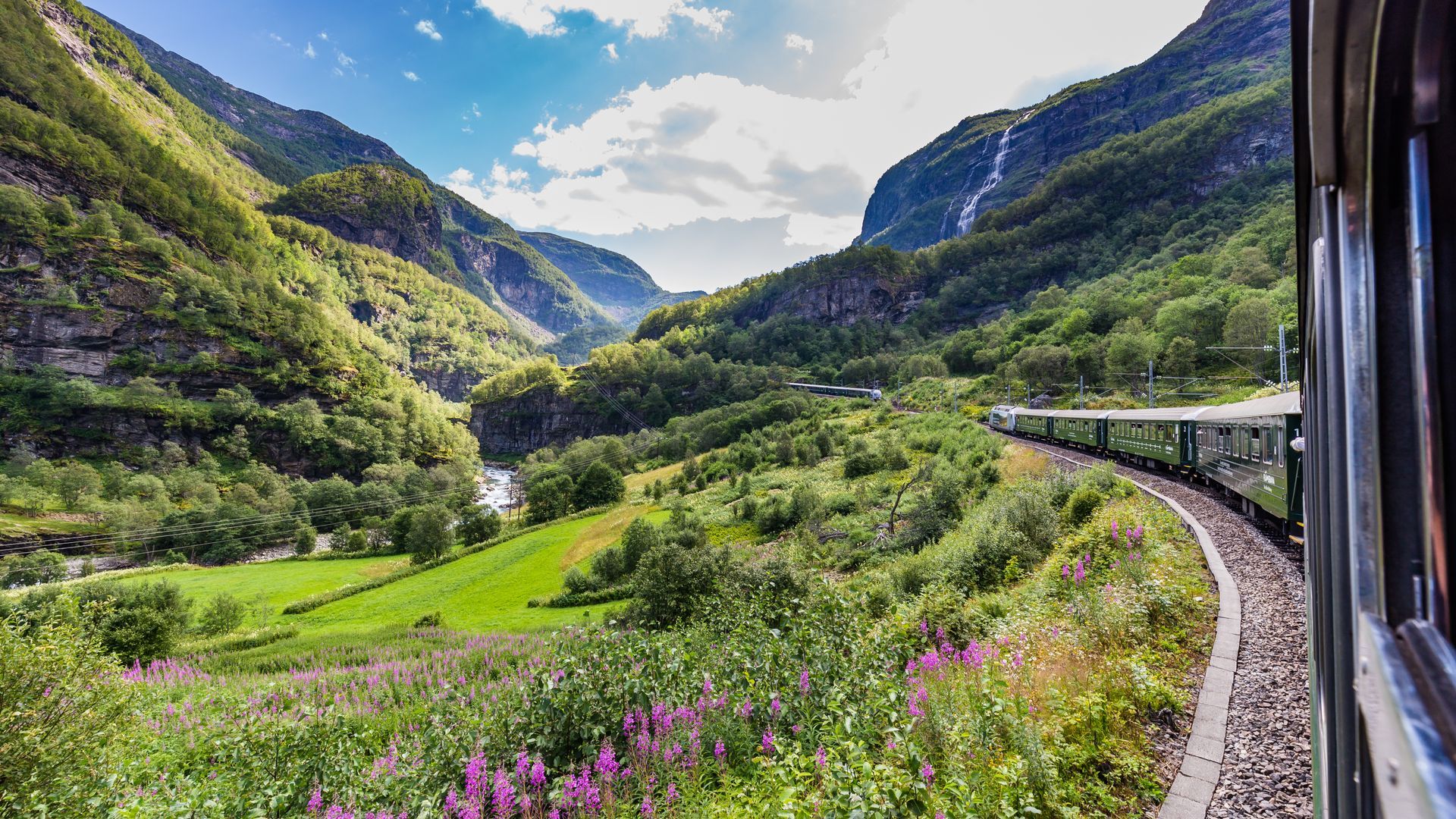 Een trein rijdt door een weelderig groen bergdal.