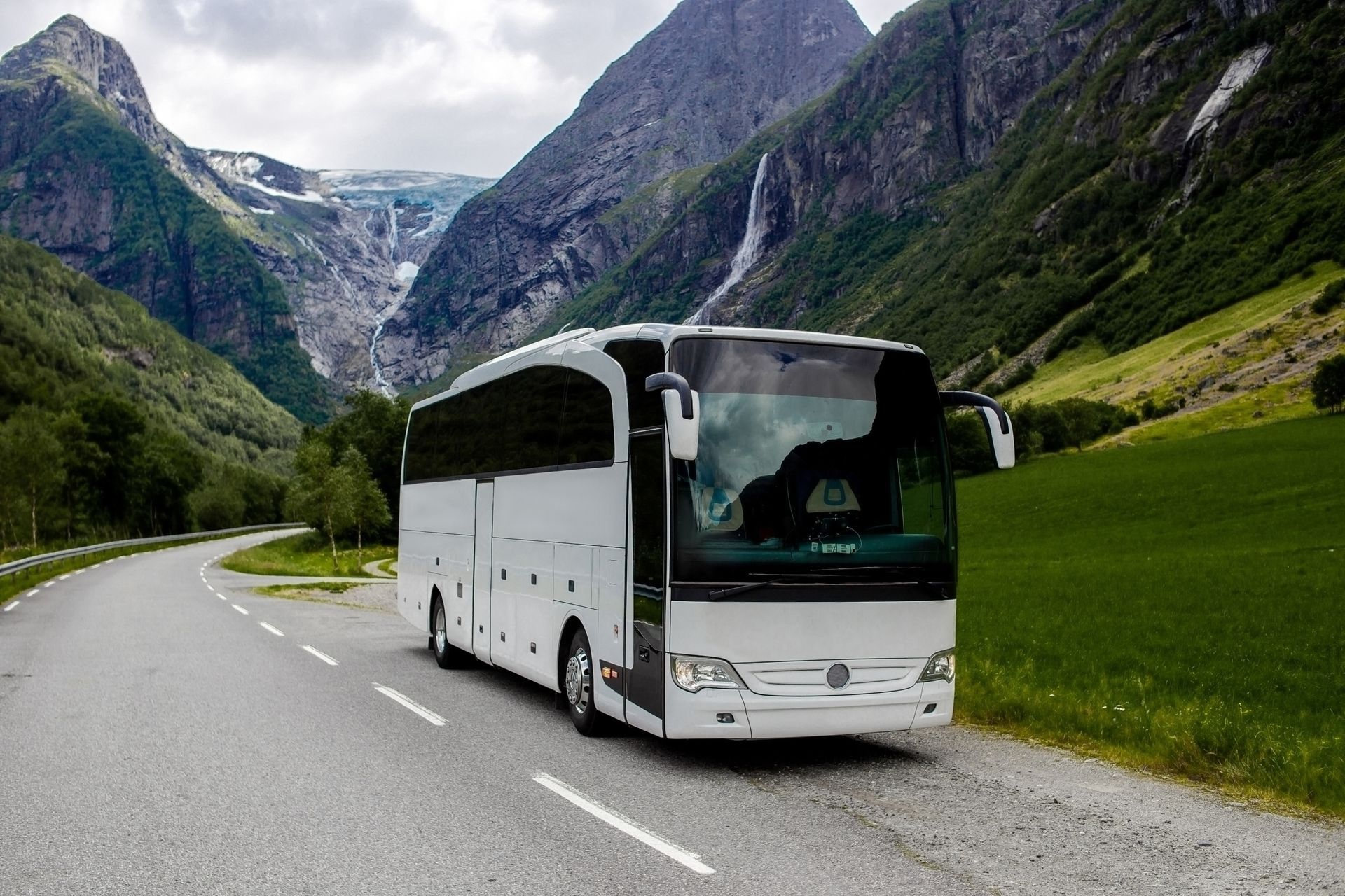 Een witte bus rijdt over een weg met bergen op de achtergrond.