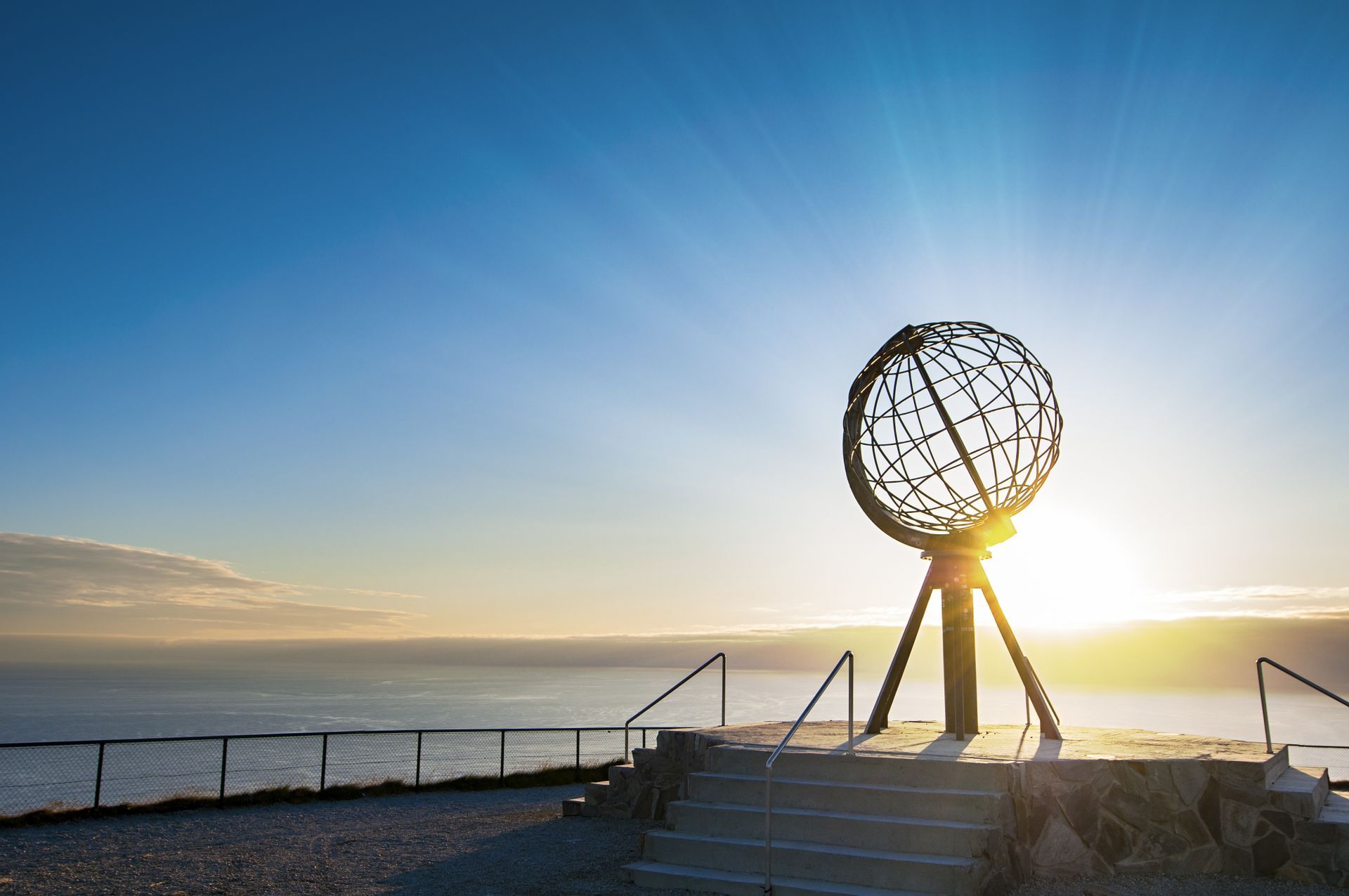 Een standbeeld van een wereldbol bovenop een heuvel met uitzicht op de oceaan bij zonsondergang.