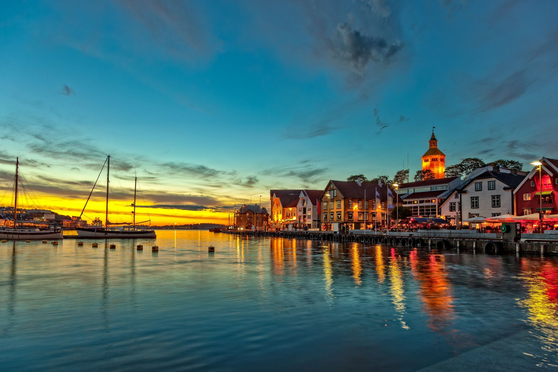 Een zonsondergang boven een haven met gebouwen en boten in het water.
