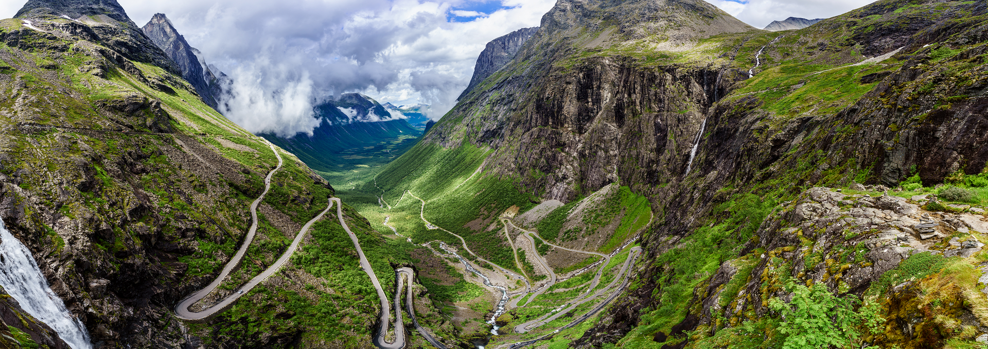 Een luchtfoto van een bergvallei met de Trollstigen erdoorheen en een waterval.