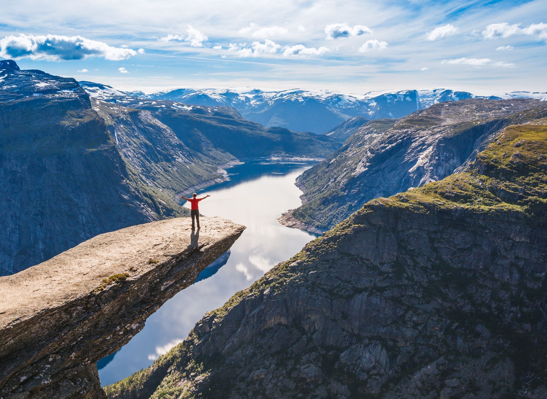 Een persoon staat op de rand van de Trolltunga met uitzicht op een fjord.