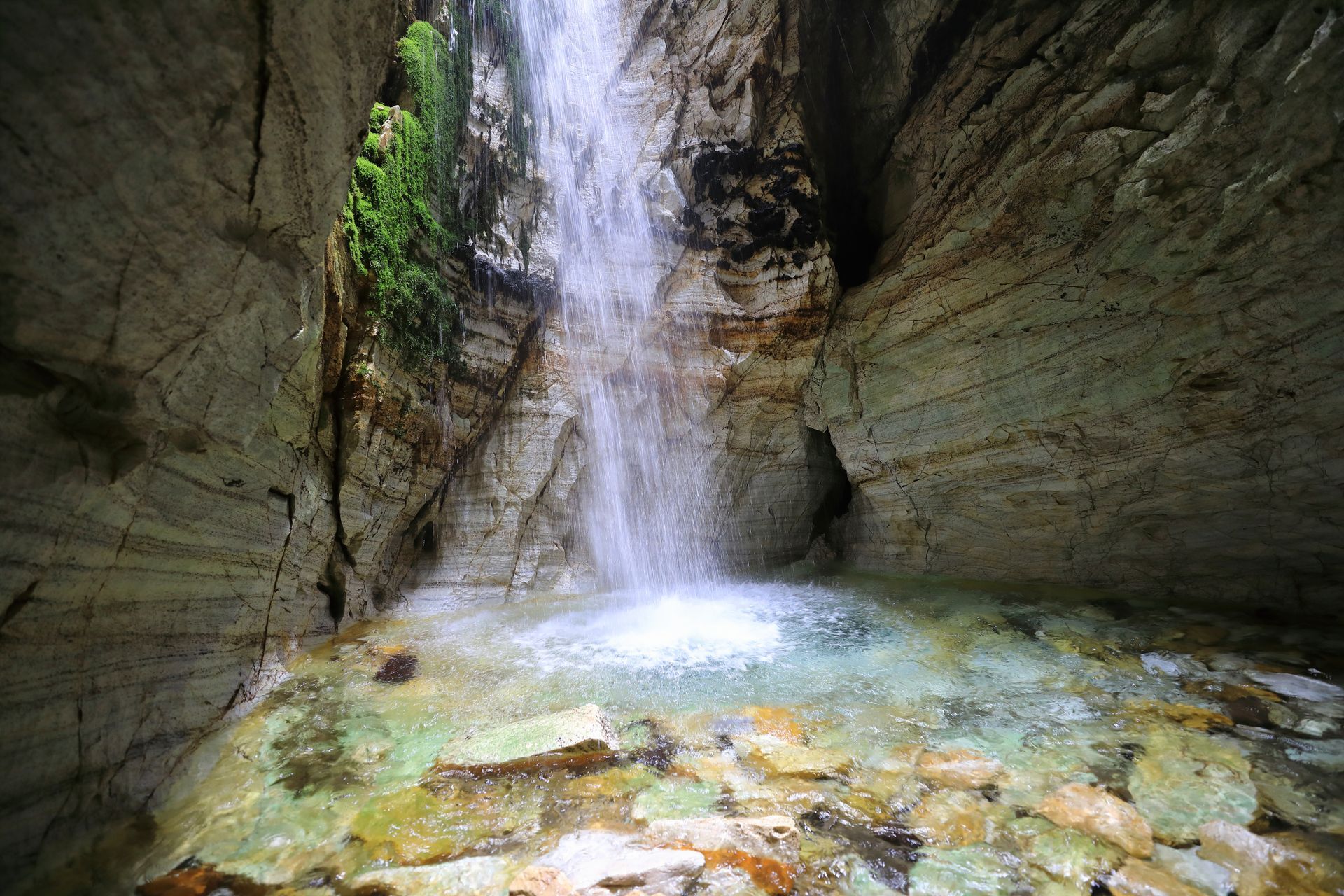 Een waterval stroomt langs een rotsachtige klif naar beneden en eindigt in een waterpoel.