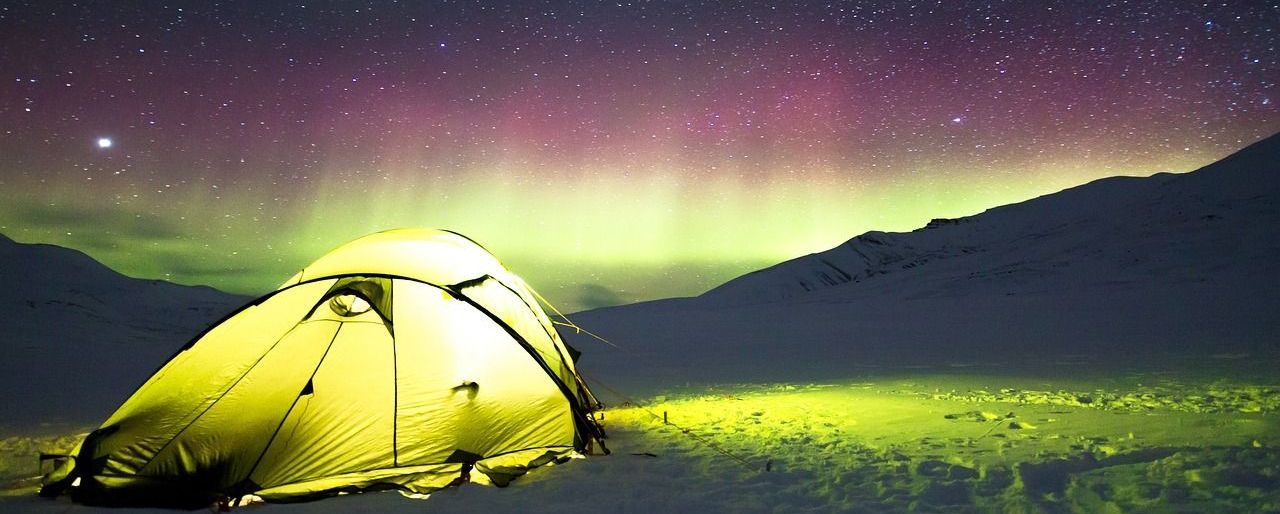 Een paarse tent staat op de top van een berg bij zonsondergang.