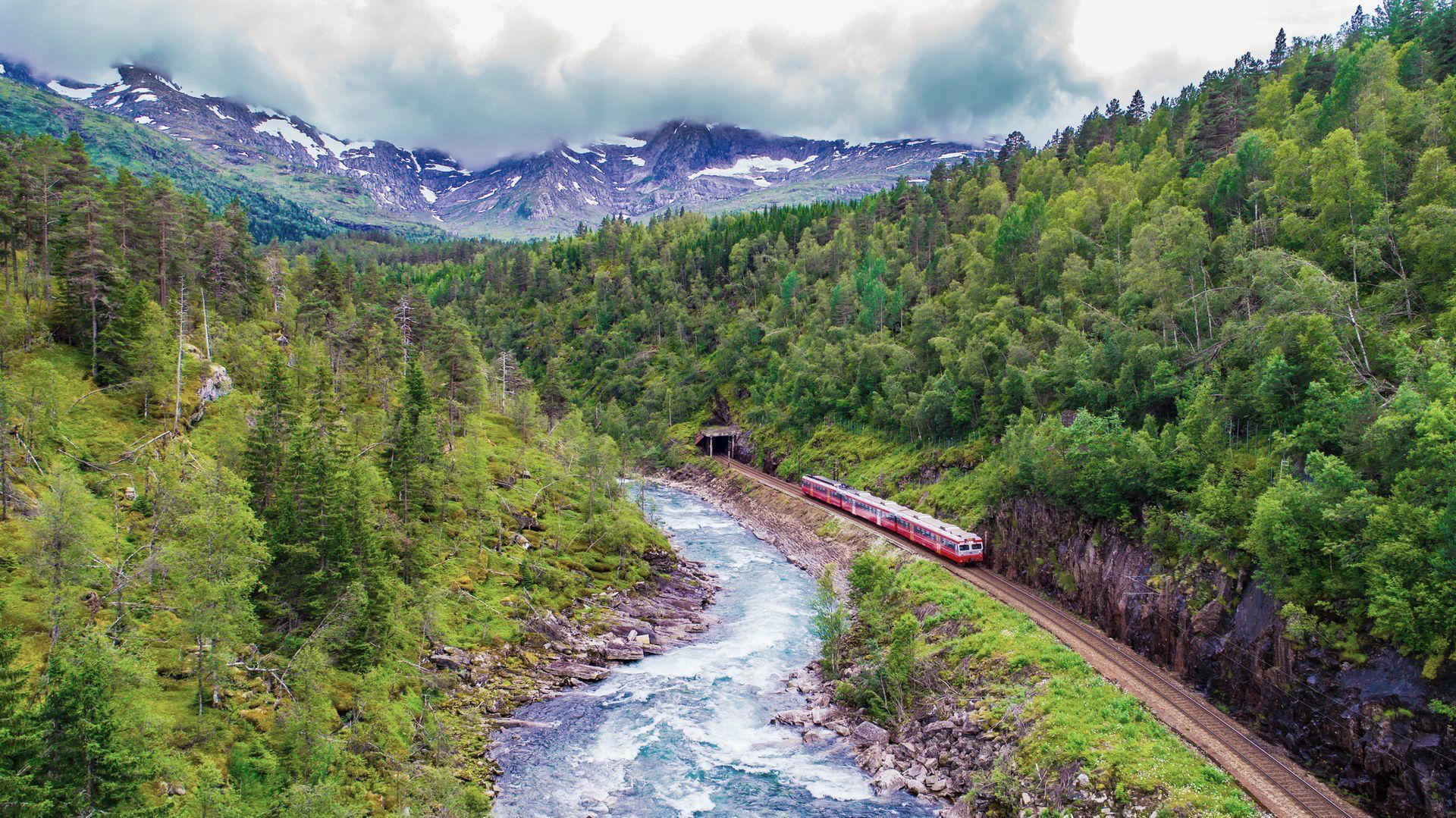 Een trein rijdt over een spoor langs een rivier in de bergen.