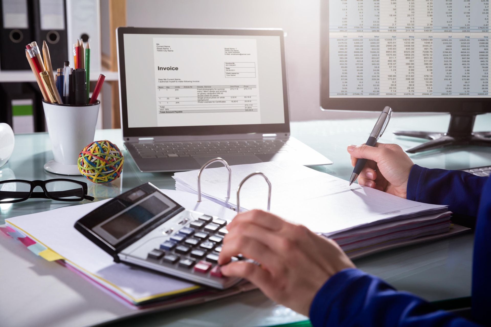 A person is sitting at a desk using a calculator and a laptop.