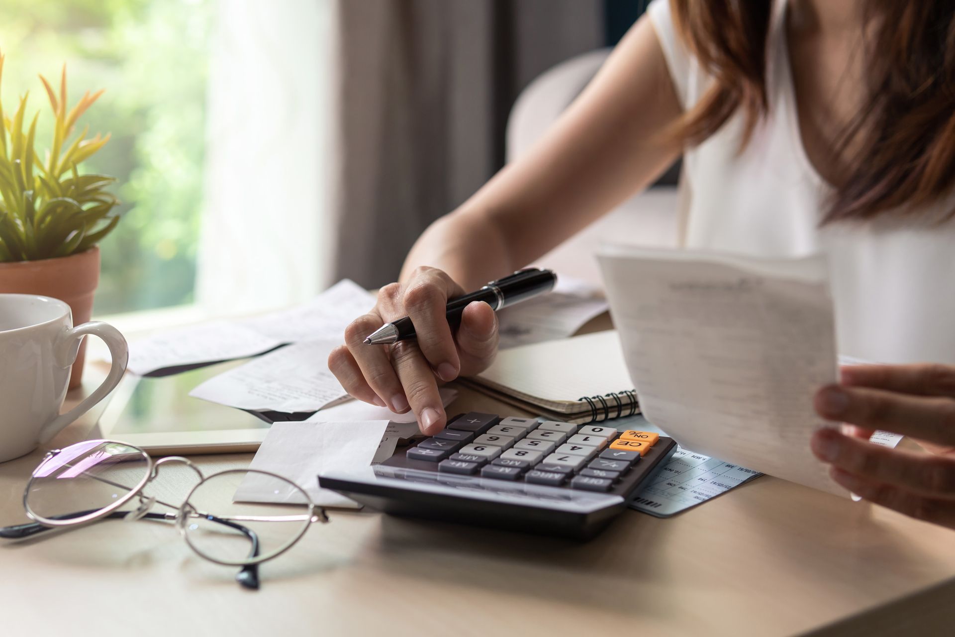 A woman is sitting at a table using a calculator and a pen.