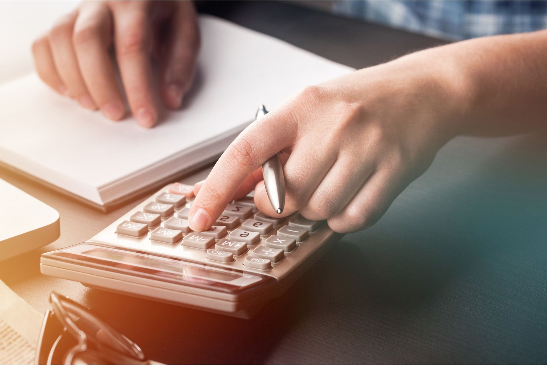 A person is using a calculator while holding a pen.