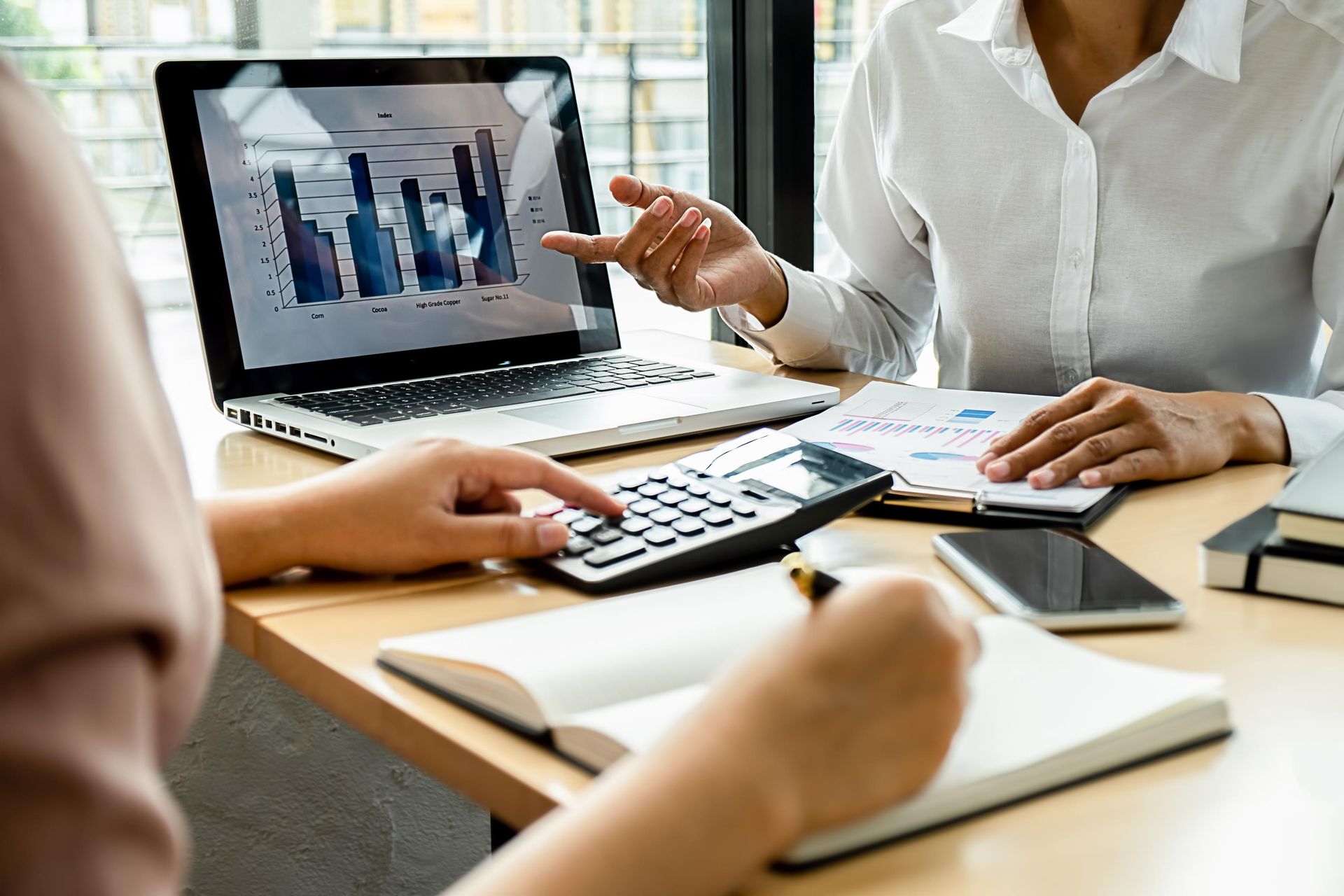 Two women are sitting at a table with a laptop and a calculator.