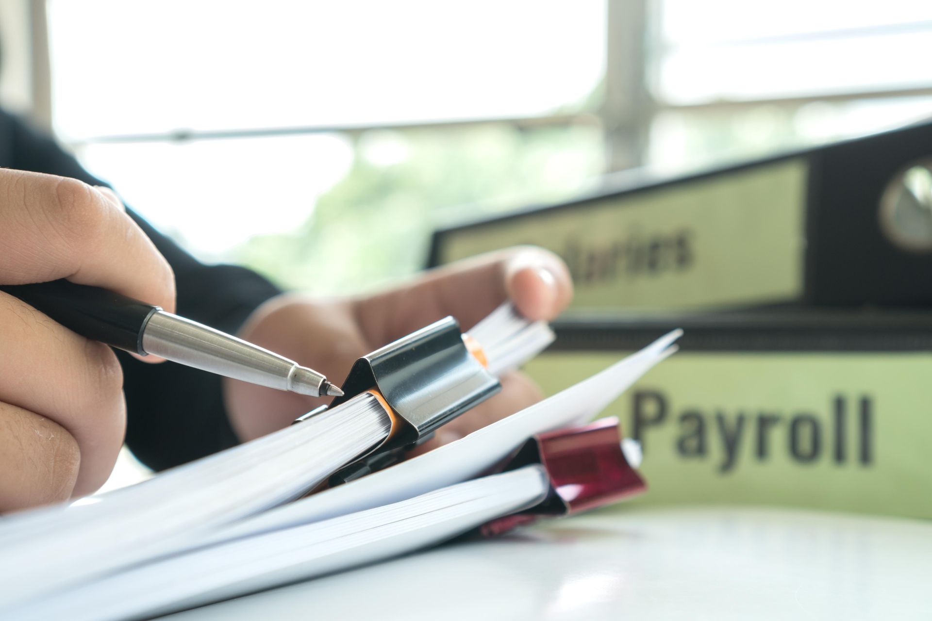 A person is holding a pen over a pile of papers.