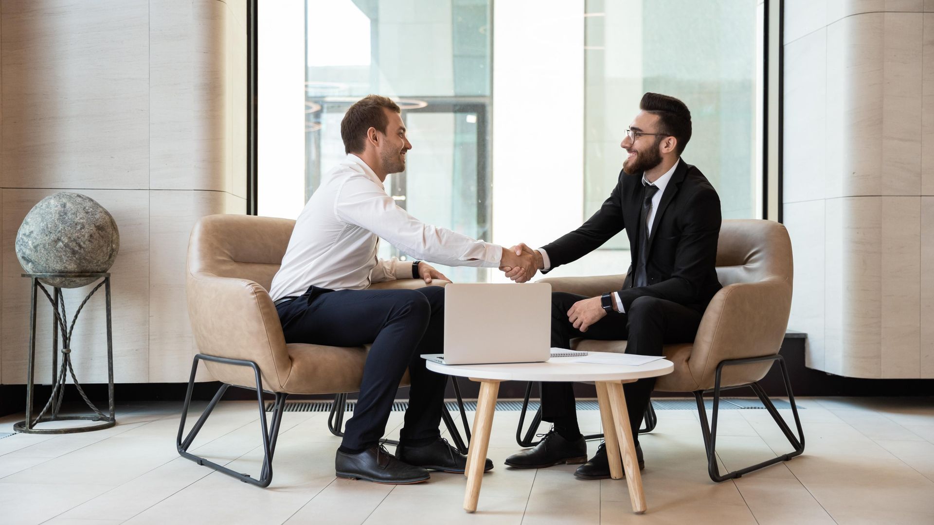 Two men are shaking hands while sitting on a couch.