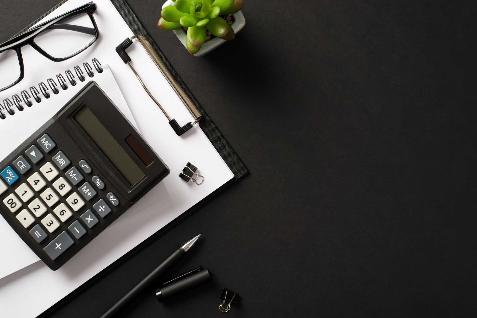 A calculator is sitting on top of a clipboard next to a pen and glasses.