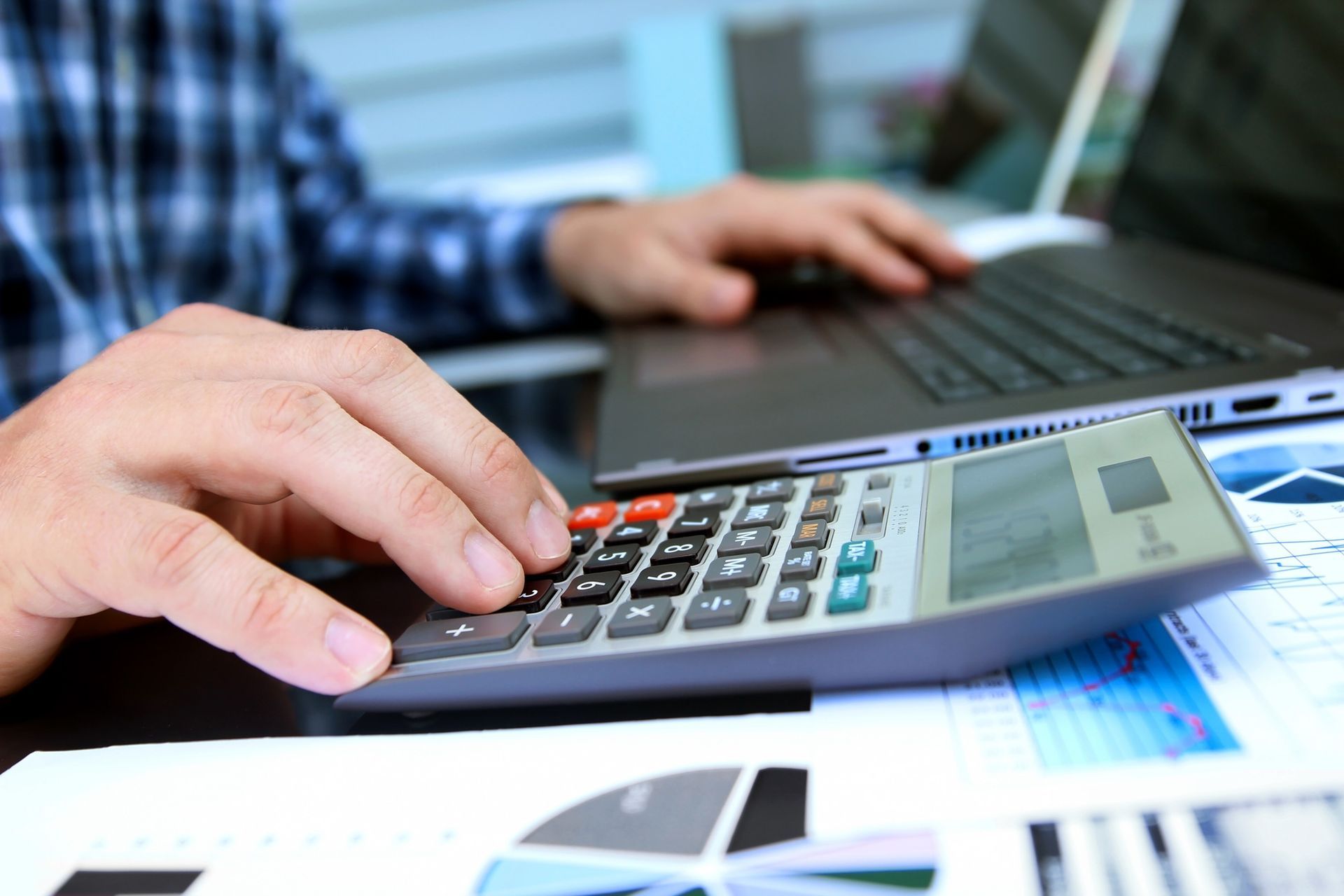 A man is using a calculator while typing on a laptop.