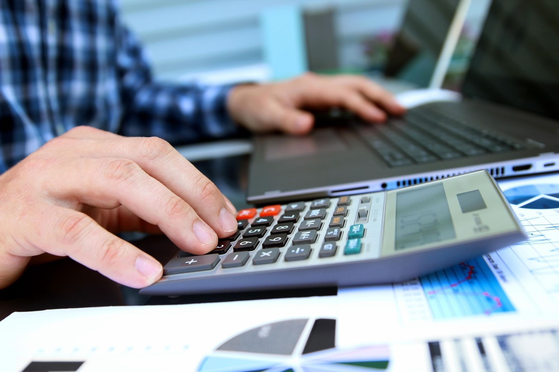 A person is using a calculator in front of a laptop computer.