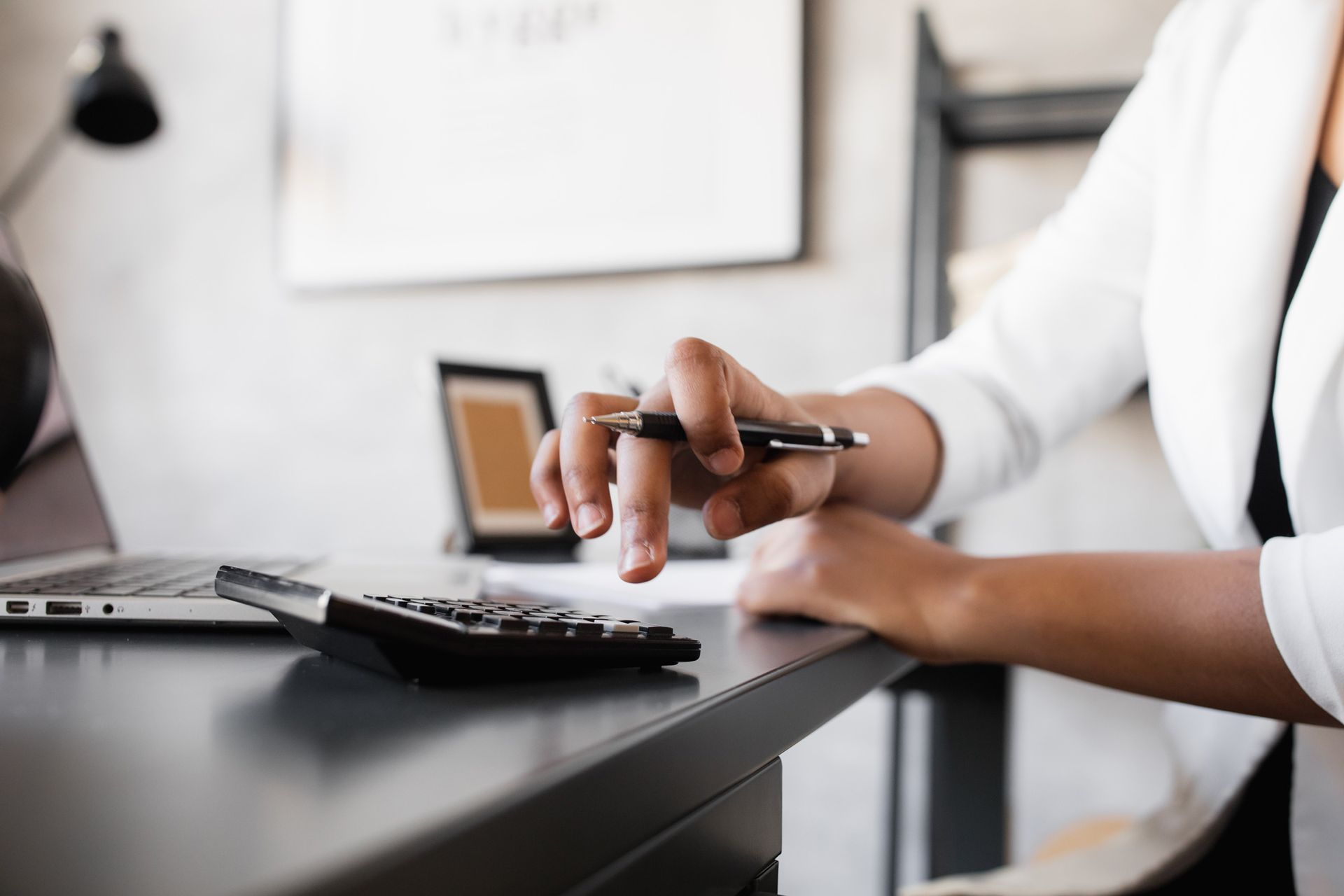 A woman is sitting at a desk using a calculator and a pen.