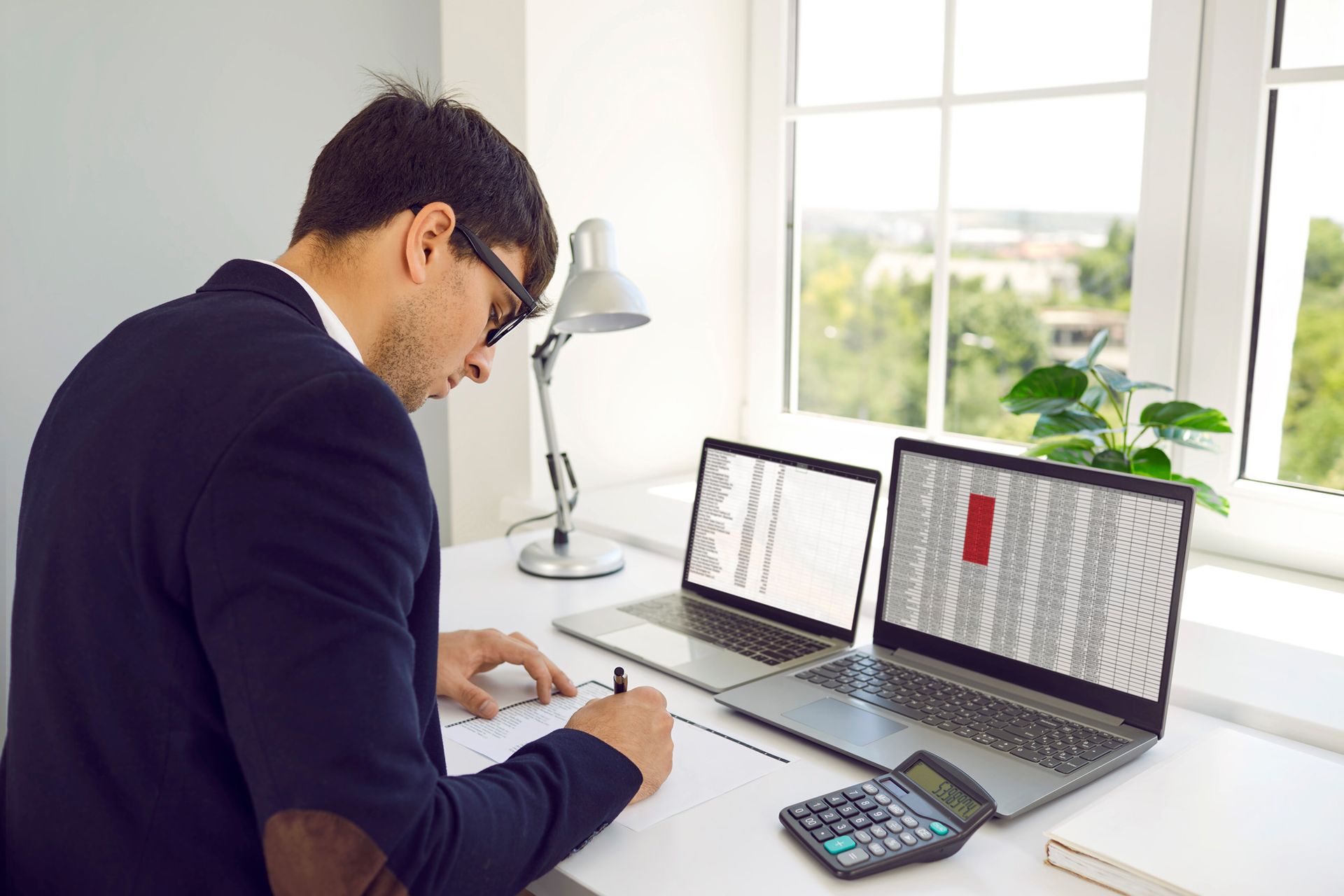 A man is sitting at a desk with two laptops and a calculator.