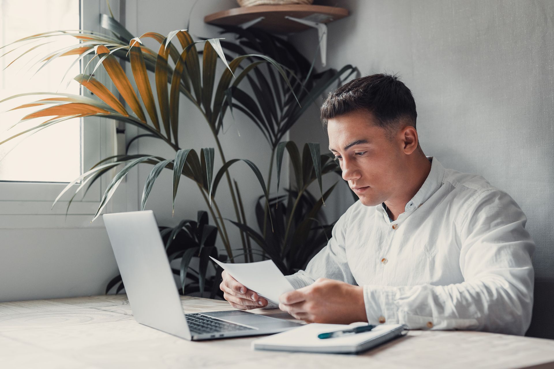 A man is sitting at a table with a laptop and a piece of paper.