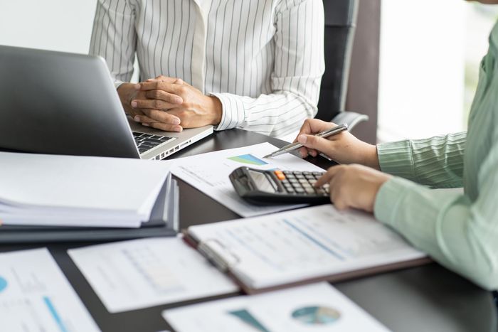 Two people are sitting at a table with a laptop and a calculator.