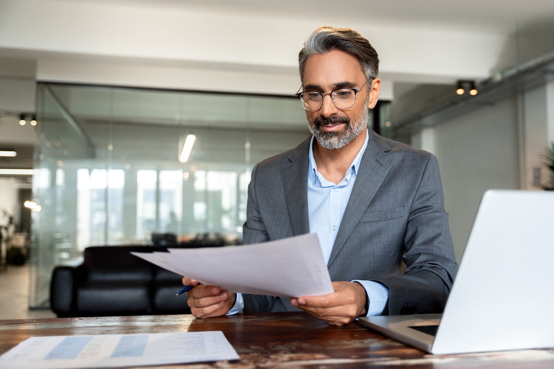 A man is sitting at a desk holding a piece of paper in front of a laptop computer.