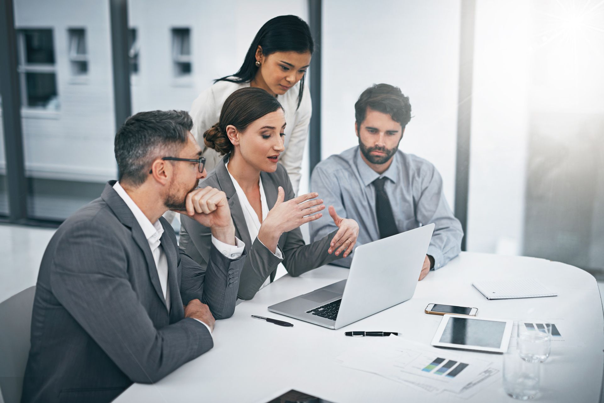 A group of business people are sitting around a table looking at a laptop computer.