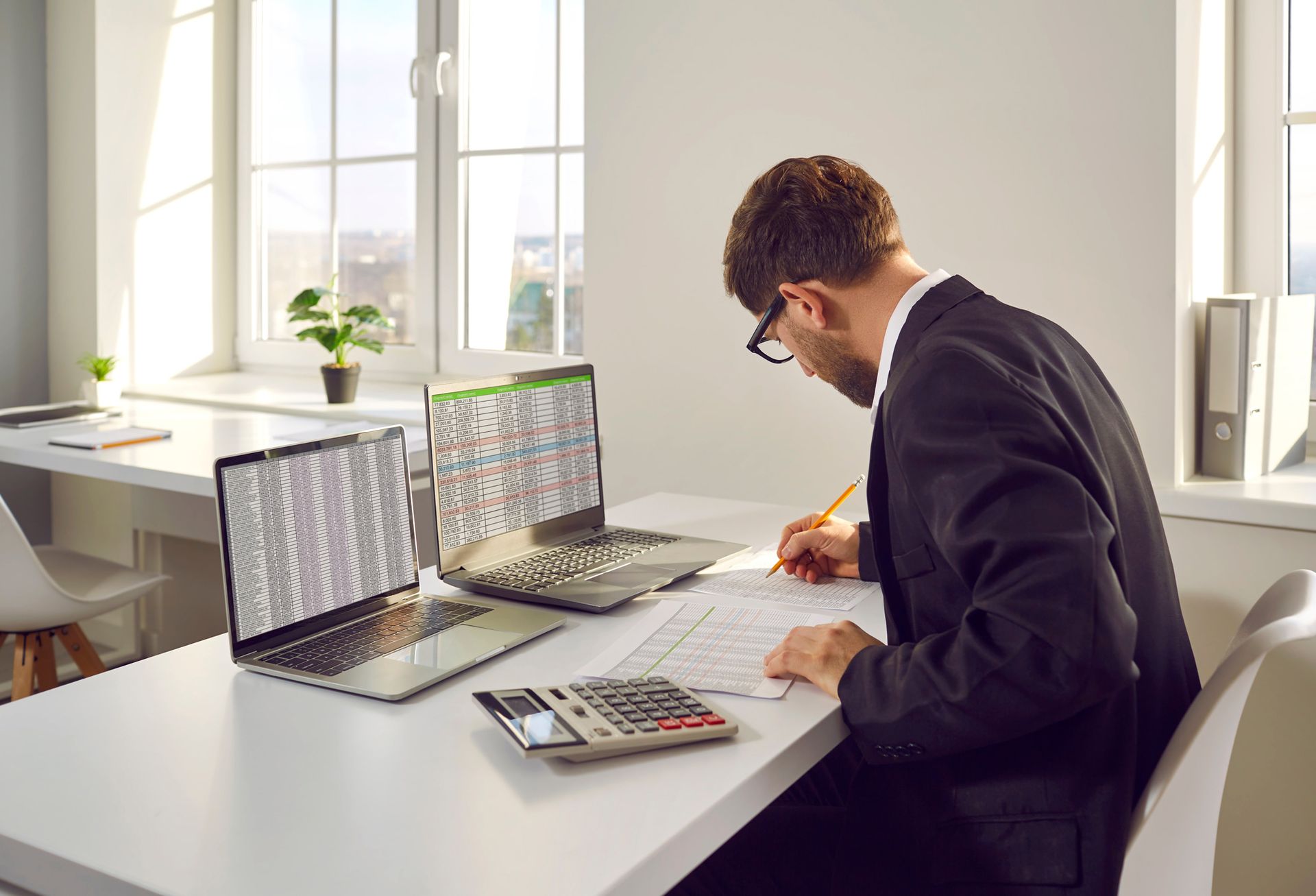 A man is sitting at a desk with two laptops and a calculator.