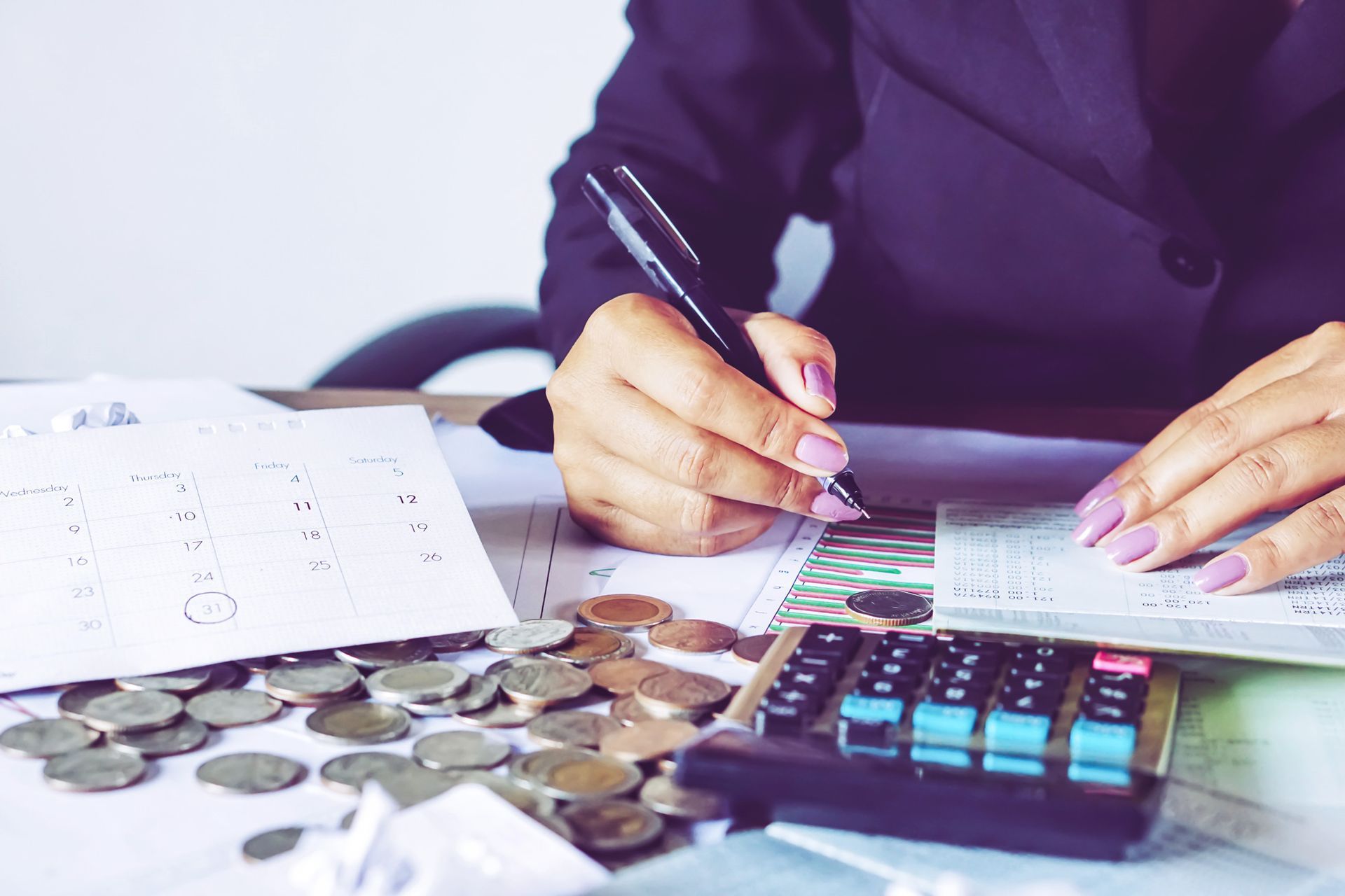 A woman is sitting at a desk using a calculator and writing on a piece of paper.