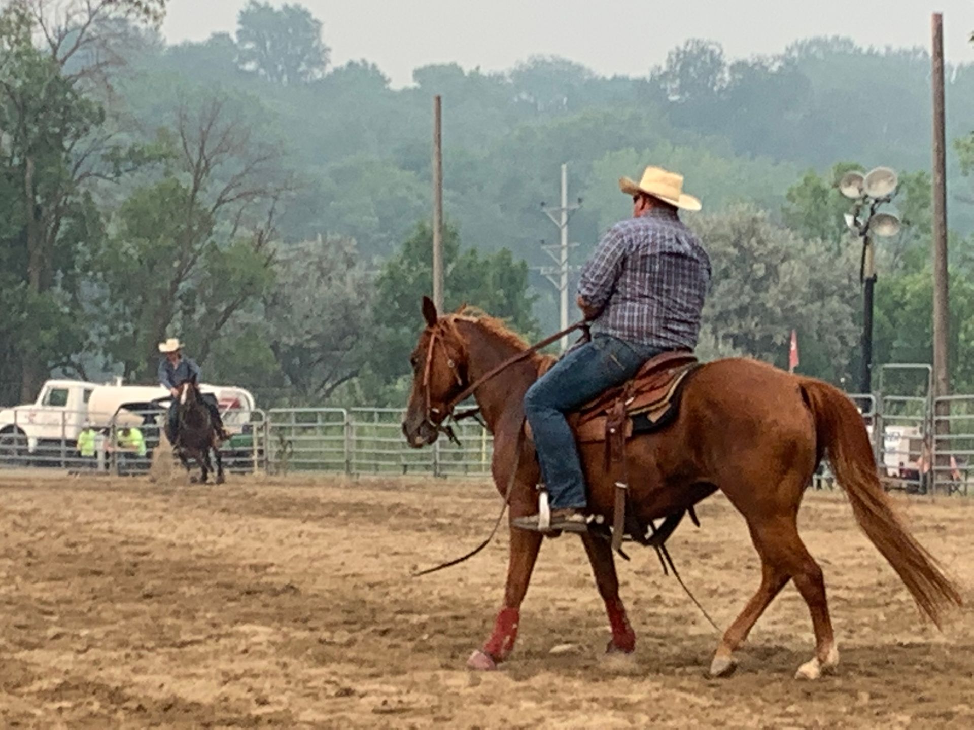 A man in a cowboy hat is riding a horse in a dirt arena.