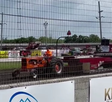 Tractor pull on a race track behind a fence.